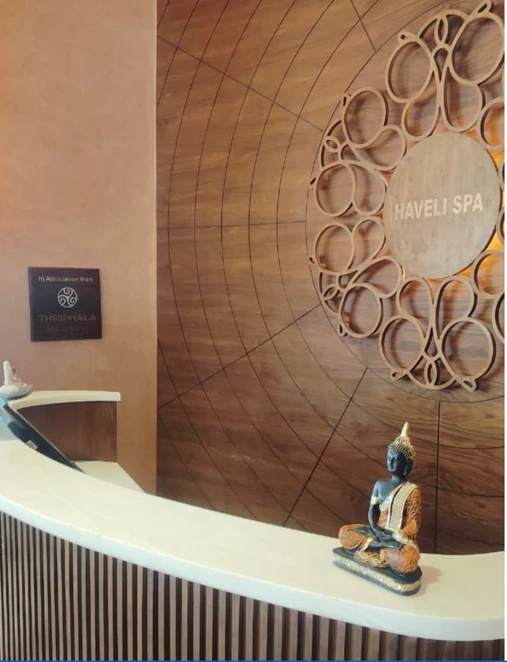 Haveli Spa reception with a carved circular wooden wall and Thriphala Wellness sign